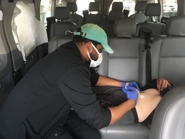 Image of Stanley Moody, L.P.N., administering a medication injection in a van. 