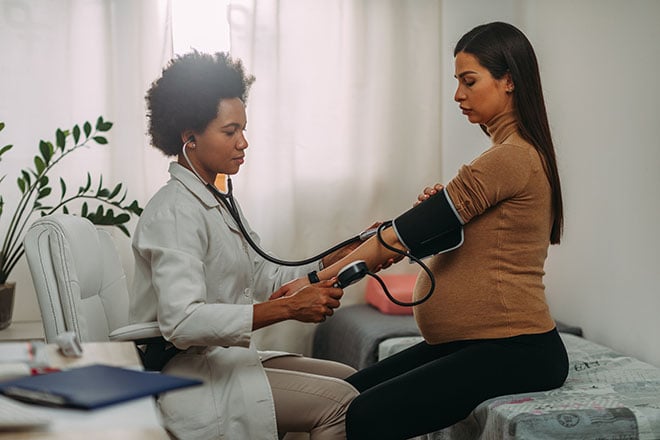 A doctor checks a pregnant person's blood pressure using a blood pressure cuff.