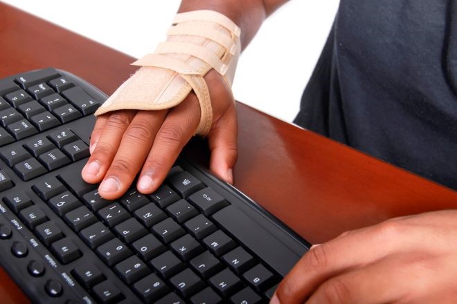 bandaged hand typing on keyboard showing carpal tunnel