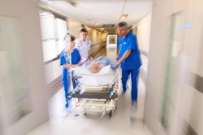 Doctors wheel a patient in a hospital bed through a hallway. The image is blurred to indicate motion.