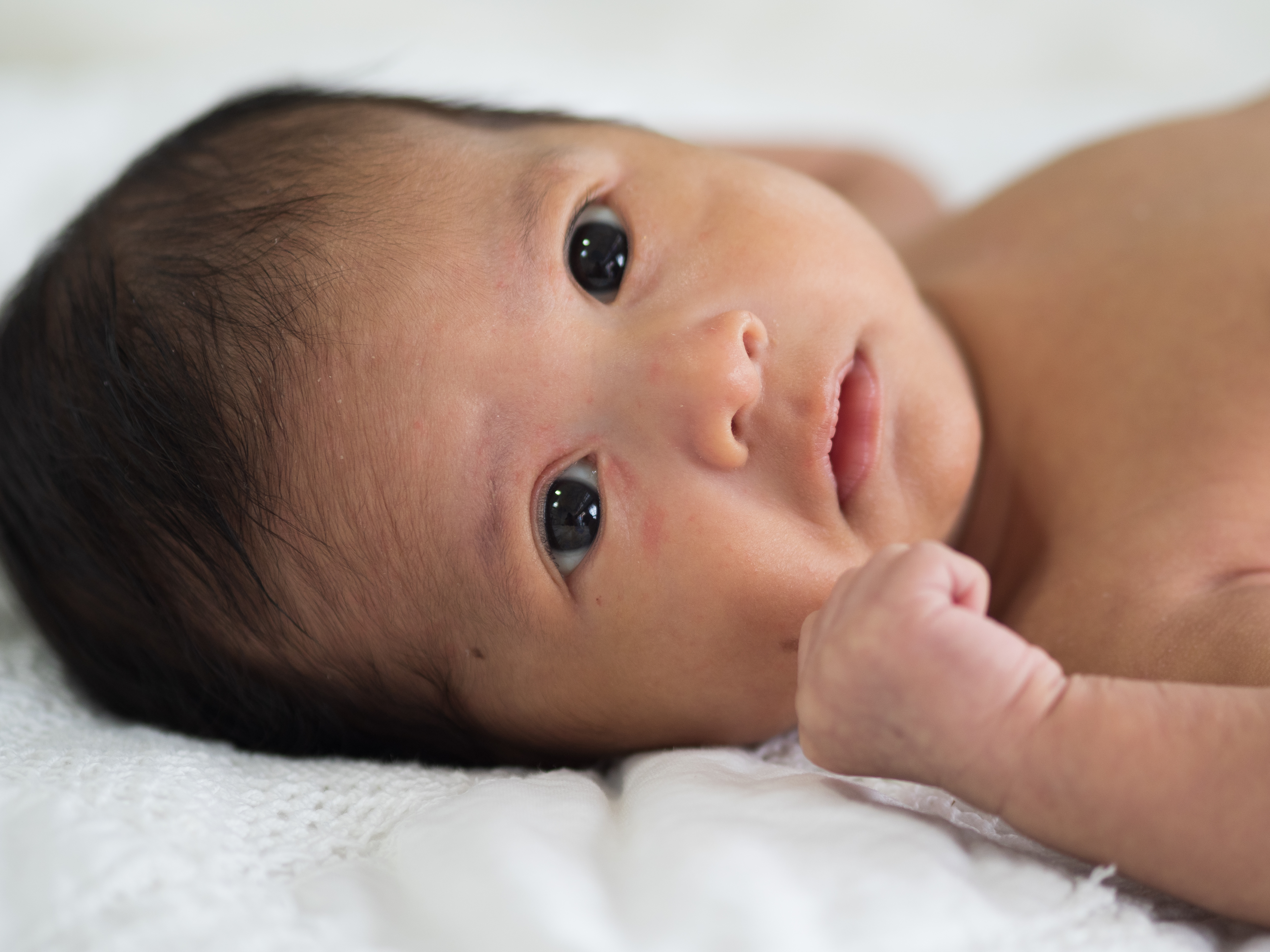 A baby lies on their back and looks off camera