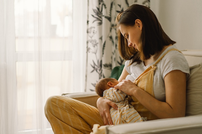 A mother sits on a chair and feeds her baby