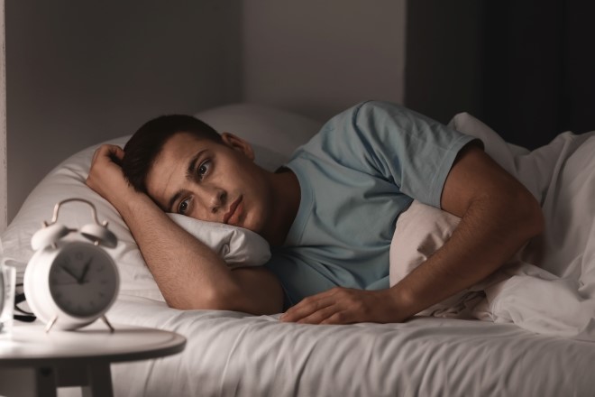 man lying in bed unable to sleep with his clock in the foreground