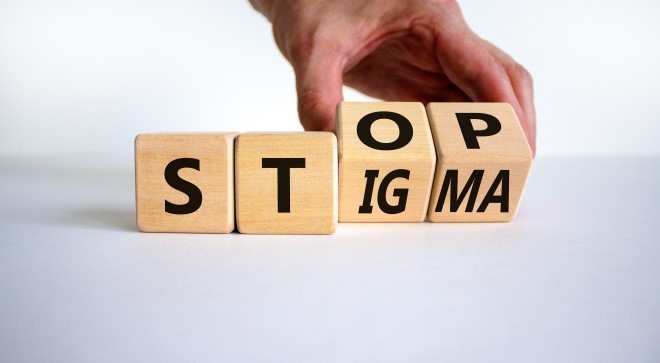 a hand turning over wooden blocks that spell out the words stigma