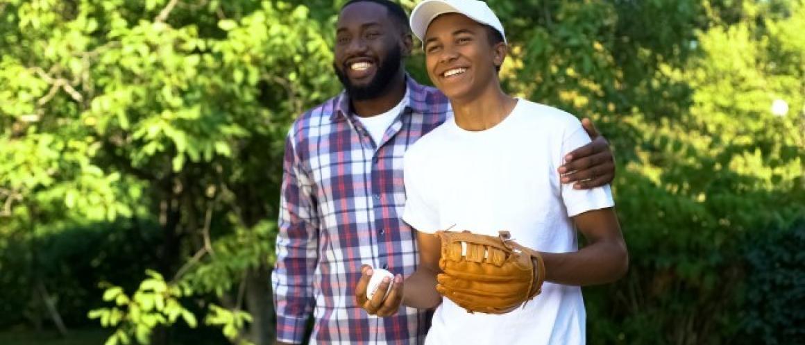 father embracing son wearing white shirt and with baseball glove and ball in hand